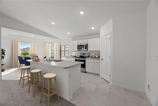 kitchen featuring a kitchen island with sink, a sink, lofted ceiling, a breakfast bar, and stainless steel appliances