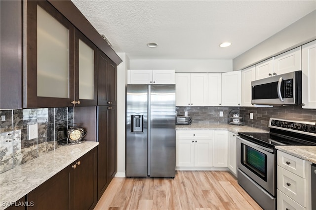 kitchen with light wood-style flooring, stainless steel appliances, white cabinetry, backsplash, and glass insert cabinets