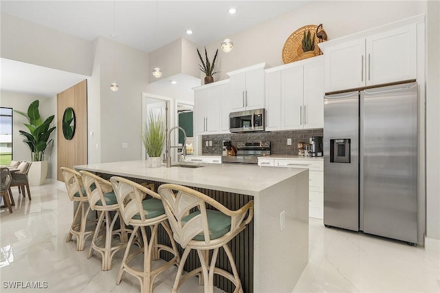 kitchen featuring a sink, a kitchen island with sink, marble finish floor, stainless steel appliances, and backsplash