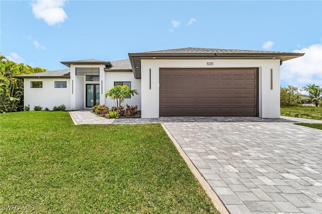 prairie-style home with a garage, a front lawn, decorative driveway, stucco siding, and french doors