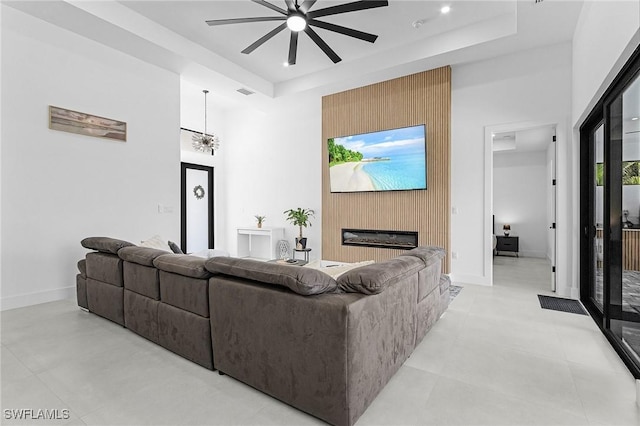 living area featuring a ceiling fan, a raised ceiling, a towering ceiling, and a fireplace