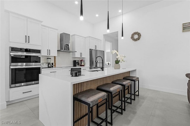 kitchen with a breakfast bar area, white cabinetry, a sink, stainless steel appliances, and wall chimney exhaust hood