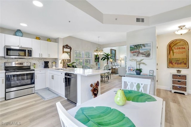 4500 Botanical Place Cir Unit 301, Naples, FL 34112 - kitchen featuring appliances with stainless steel finishes, a sink, white cabinets, a peninsula, and a notable chandelier