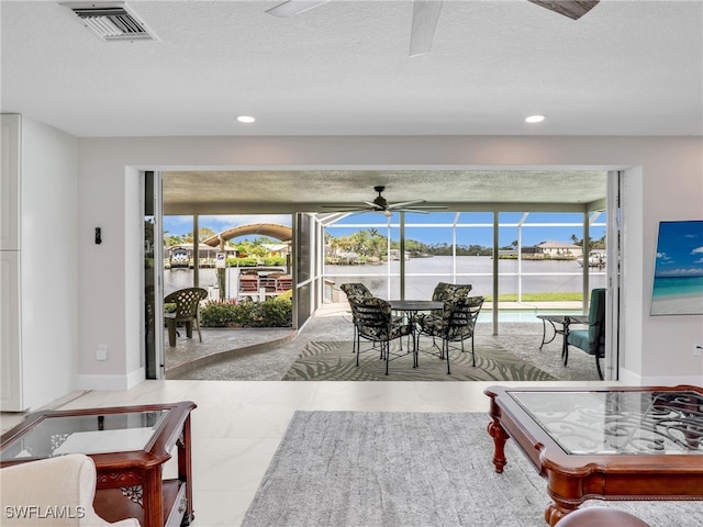 living area featuring a ceiling fan, a water view, baseboards, a textured ceiling, and recessed lighting