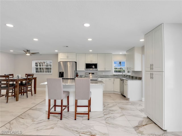 kitchen featuring appliances with stainless steel finishes, recessed lighting, a center island, light marble finish flooring, and a ceiling fan