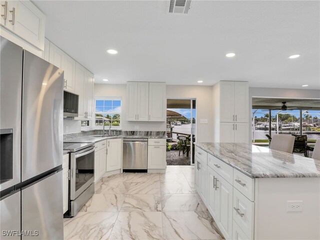 kitchen featuring stainless steel appliances, a sink, white cabinets, light marble finish flooring, and light stone countertops