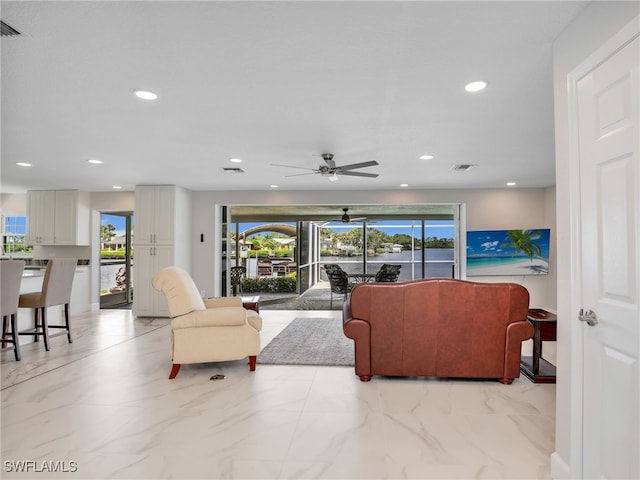 living area with recessed lighting, plenty of natural light, a ceiling fan, and light marble finish floors