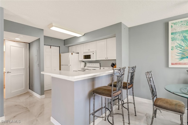 kitchen featuring a kitchen breakfast bar, baseboards, marble finish floor, white appliances, and white cabinetry