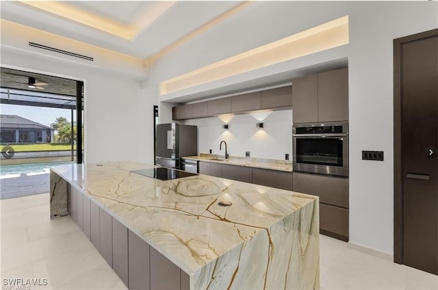 kitchen with light stone countertops, a large island, modern cabinets, appliances with stainless steel finishes, and gray cabinetry