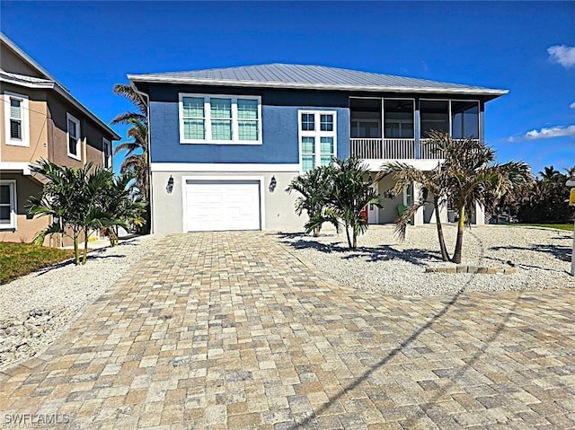 beach home featuring a garage, stucco siding, a sunroom, decorative driveway, and metal roof