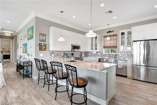kitchen with visible vents, a peninsula, a breakfast bar, glass insert cabinets, and appliances with stainless steel finishes