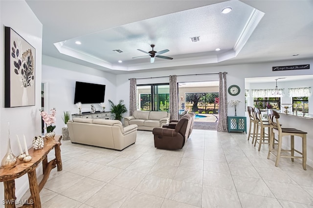 living room featuring a tray ceiling, visible vents, and ceiling fan