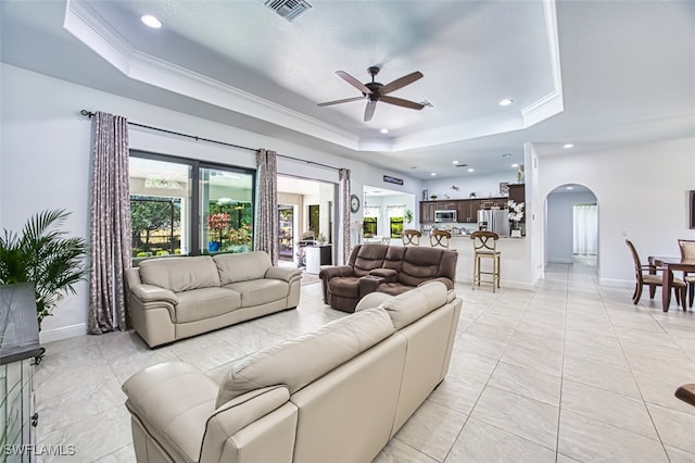 living area with ceiling fan, a raised ceiling, arched walkways, a wealth of natural light, and visible vents