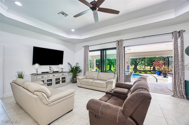 living area with a raised ceiling, a ceiling fan, light tile patterned floors, visible vents, and ornamental molding