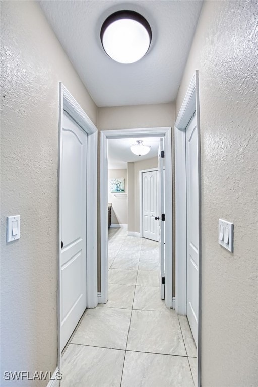 hallway featuring a textured wall and light tile patterned floors