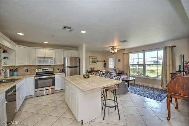 kitchen with visible vents, appliances with stainless steel finishes, open shelves, a sink, and a breakfast bar