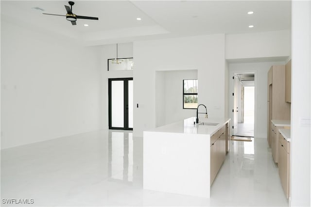 kitchen with a ceiling fan, modern cabinets, a center island with sink, a sink, and light countertops