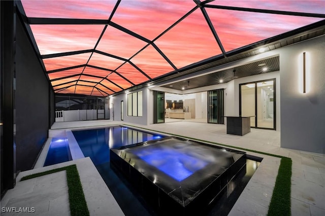 back of house featuring glass enclosure, a patio area, stucco siding, and a pool with connected hot tub