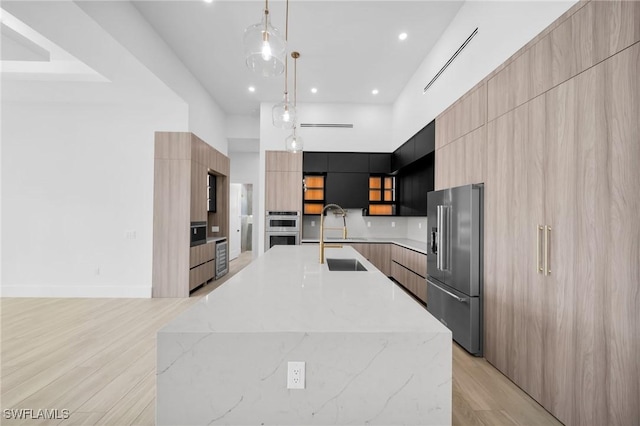 kitchen with appliances with stainless steel finishes, a sink, light wood finished floors, a towering ceiling, and modern cabinets