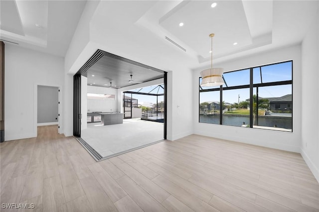 interior space with wood finished floors, baseboards, recessed lighting, a water view, and a tray ceiling