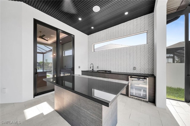 kitchen with dark countertops, a sink, beverage cooler, recessed lighting, and backsplash