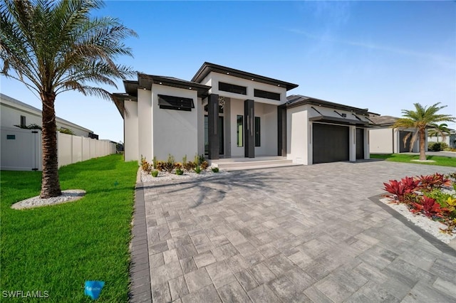 prairie-style house featuring fence, an attached garage, stucco siding, a front yard, and decorative driveway