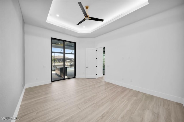 spare room with baseboards, a tray ceiling, ceiling fan, and light wood finished floors