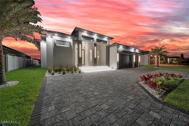 view of front of home with fence, an attached garage, stucco siding, decorative driveway, and a lawn