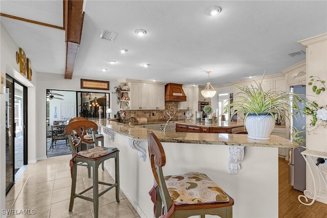 kitchen with a kitchen breakfast bar, decorative backsplash, premium range hood, beam ceiling, and refrigerator