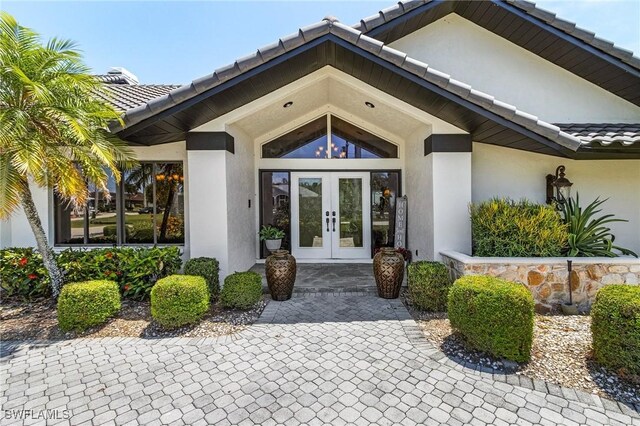 entrance to property with french doors, a tile roof, and stucco siding