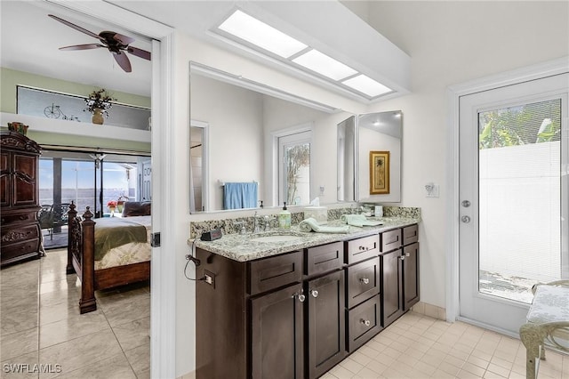 full bathroom with ensuite bath, double vanity, tile patterned floors, a ceiling fan, and baseboards