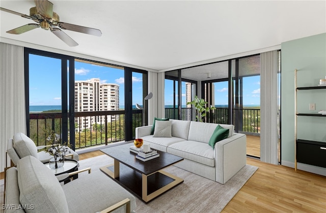 living area featuring a ceiling fan, light wood finished floors, and expansive windows