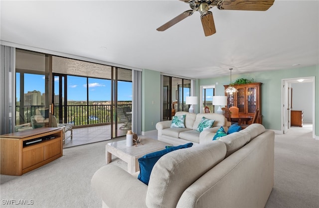 living area featuring a wall of windows, baseboards, ceiling fan, and light colored carpet