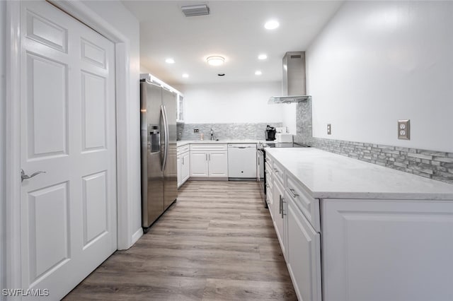 kitchen with white cabinets, wall chimney exhaust hood, stainless steel appliances, backsplash, and visible vents
