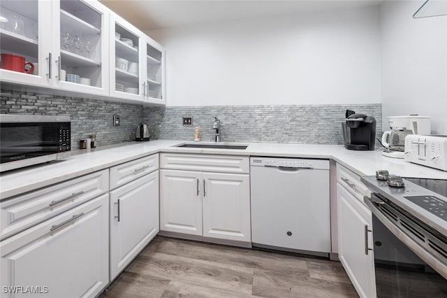 kitchen with backsplash, appliances with stainless steel finishes, a sink, glass insert cabinets, and white cabinetry