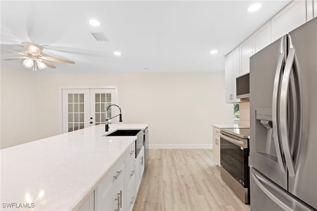 kitchen with light wood-type flooring, white cabinets, french doors, a sink, and stainless steel appliances