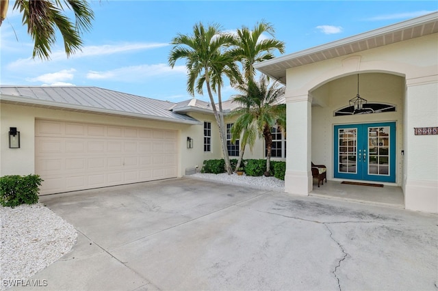 view of exterior entry featuring concrete driveway, a garage, french doors, and stucco siding