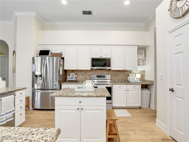 kitchen featuring appliances with stainless steel finishes, white cabinetry, tasteful backsplash, visible vents, and ornamental molding