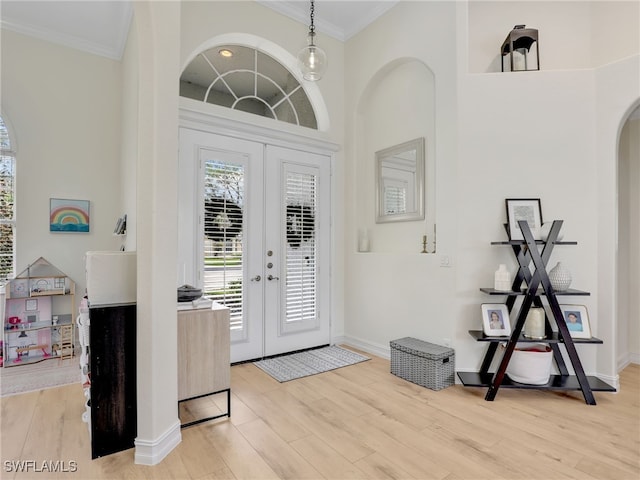 foyer featuring crown molding, light wood-style floors, baseboards, french doors, and arched walkways