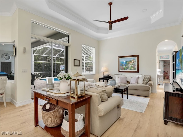 living room with a ceiling fan, ornamental molding, light wood-type flooring, a raised ceiling, and arched walkways