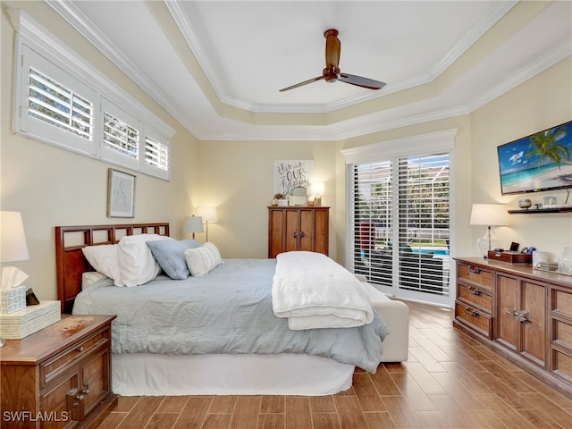 bedroom featuring ceiling fan, access to exterior, wood finished floors, ornamental molding, and a tray ceiling