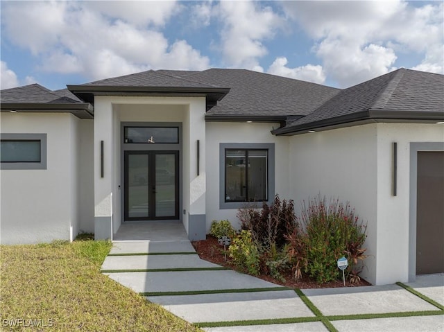 view of exterior entry featuring french doors, stucco siding, and roof with shingles