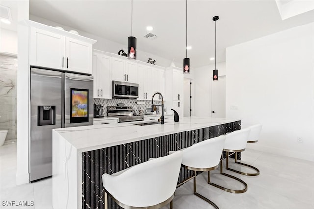 kitchen featuring white cabinets, light stone counters, an island with sink, stainless steel appliances, and visible vents