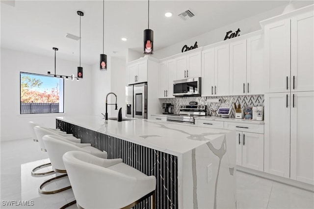 kitchen featuring visible vents, a sink, stainless steel appliances, white cabinetry, and an island with sink