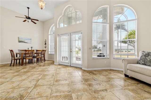interior space with baseboards, ceiling fan, and a high ceiling