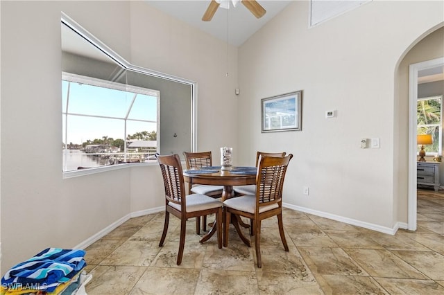 dining area with arched walkways, ceiling fan, baseboards, and high vaulted ceiling