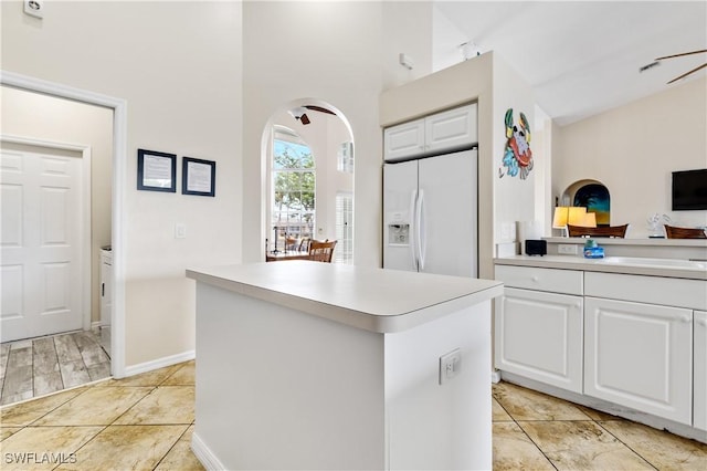 kitchen with a kitchen island, white refrigerator with ice dispenser, light countertops, white cabinets, and arched walkways