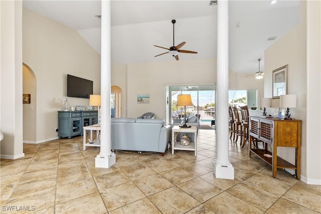 tiled living area featuring arched walkways, ceiling fan, ornate columns, and high vaulted ceiling