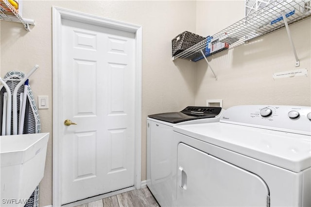 laundry area featuring separate washer and dryer, laundry area, baseboards, and light wood finished floors