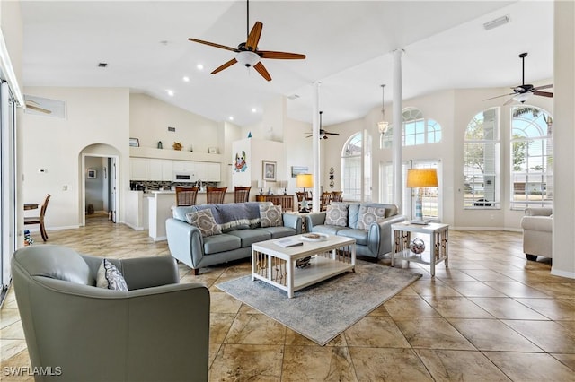 living room with visible vents, baseboards, high vaulted ceiling, arched walkways, and a ceiling fan